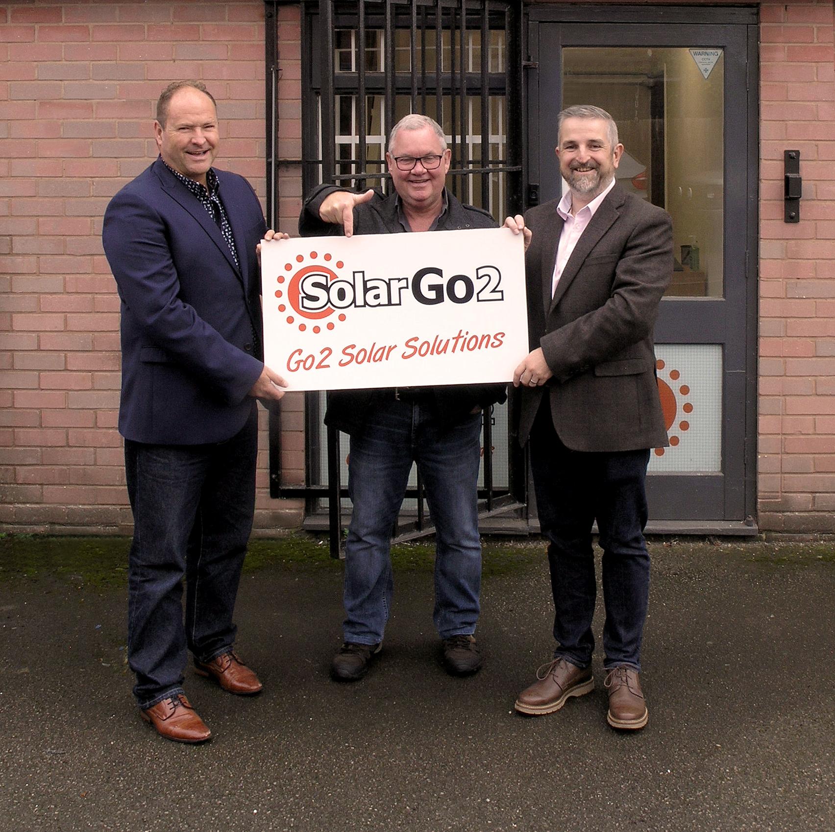 The SolarGo2 team, stood outside their new unit, holding a SolarGo2 sign. The sign reads: SolarGo2 - Go2 Solar Solutions